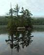 The fog has mostly broken leaving a nearly perfect island reflection and a mist in the hills across the lake.